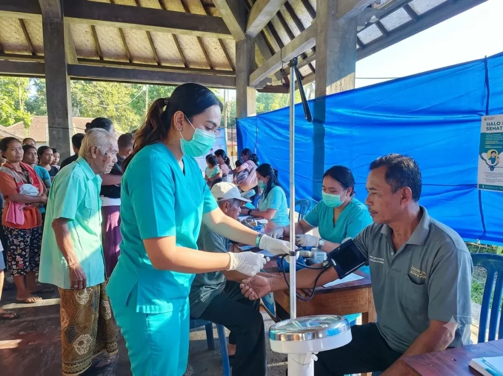 A Bali Sehat Clinic nurse checking an elderly man's blood pressure during Healthy Day in Desa Kesimpar