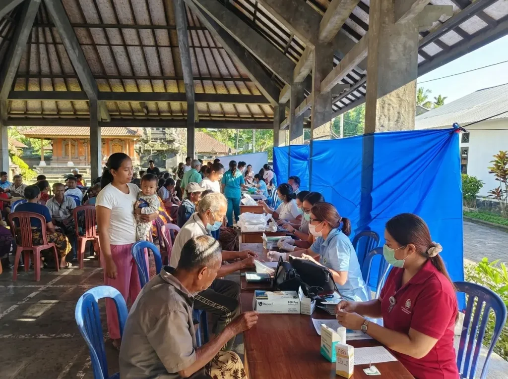 Bali Sehat Clinic medical staff conducting health tests for villagers at outdoor tables during Healthy Day in Desa Kesimpar