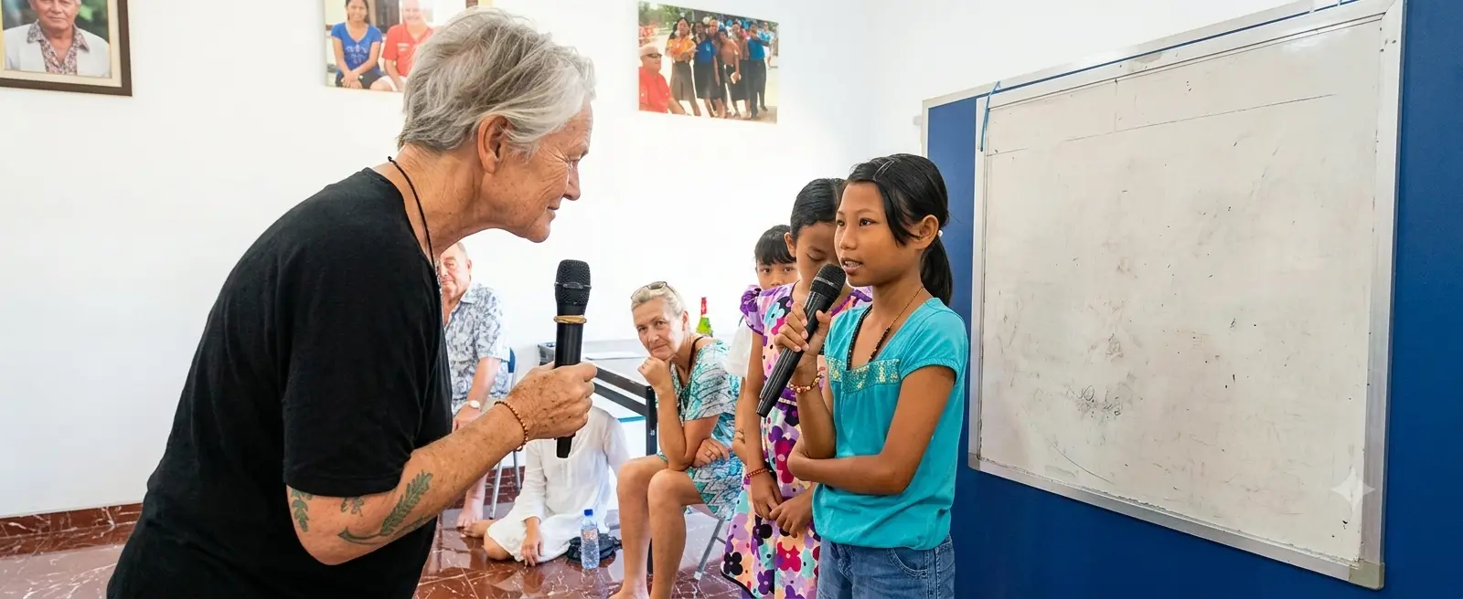 A volunteer encourages a young girl holding a microphone to speak English during Fun English Day at Bali Sehat Clinic