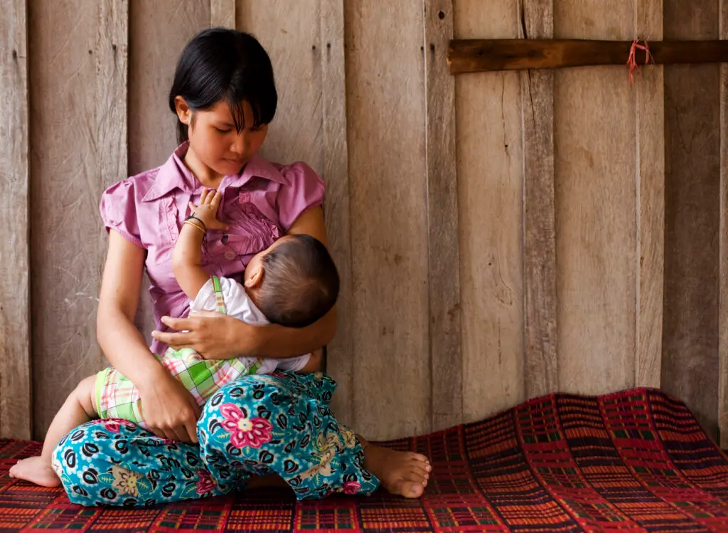 Mother breastfeeding her baby while sitting on a traditional woven mat