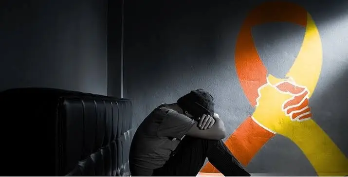 World Suicide Prevention Day – Bali Sehat A man sitting on the floor with his head down, next to a suicide prevention awareness ribbon, marking World Suicide Prevention Day