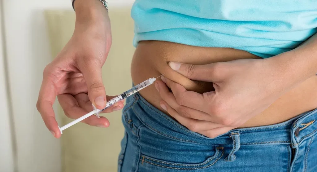 Person pinching the skin of the abdomen while holding an insulin syringe