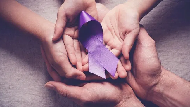 Several hands holding a purple ribbon, the colour of pancreatic cancer awareness